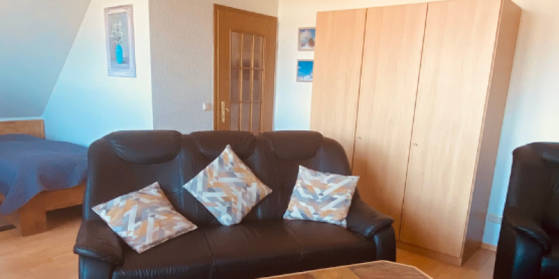 Schwarze Ledercouch mit Schrank im Hintergrund und Fliesentisch vor dem Sofa. Bett in der ecke